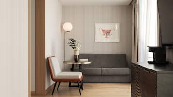 A modern living room with a grey sofa, a wooden floor, a round table with a vase of flowers, and a framed picture on the wall.