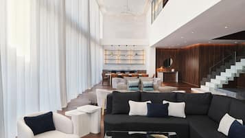 Un amplio espacio de sala con un sofá oscuro, un sillón blanco y una mesa de centro de vidrio.