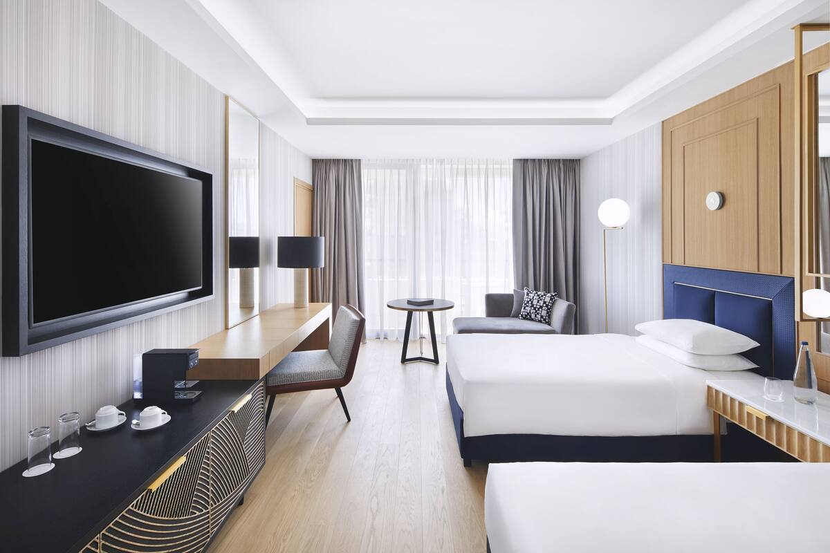 Une chambre d’hôtel moderne équipée d’une télévision à écran plat, d’un bureau avec une machine à café, d’un canapé, d’un lit et d’une table ronde.
