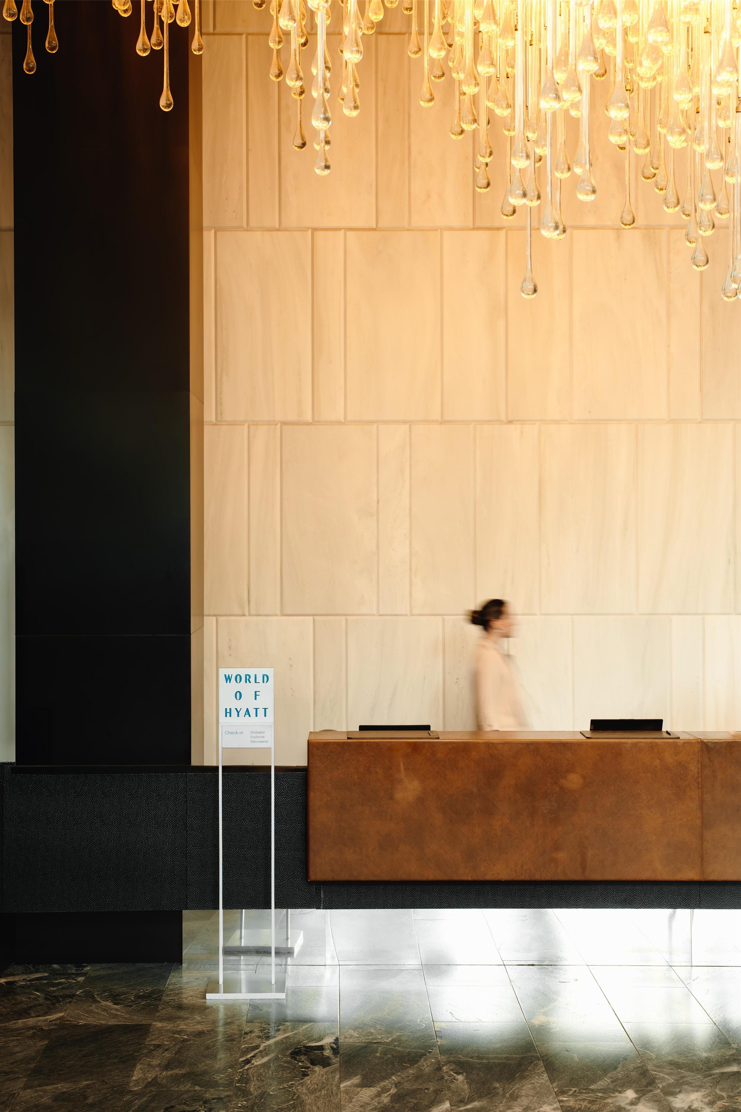 A hotel reception area with a marble floor, a wooden reception desk, and a sign indicating 'World of Hyatt'.