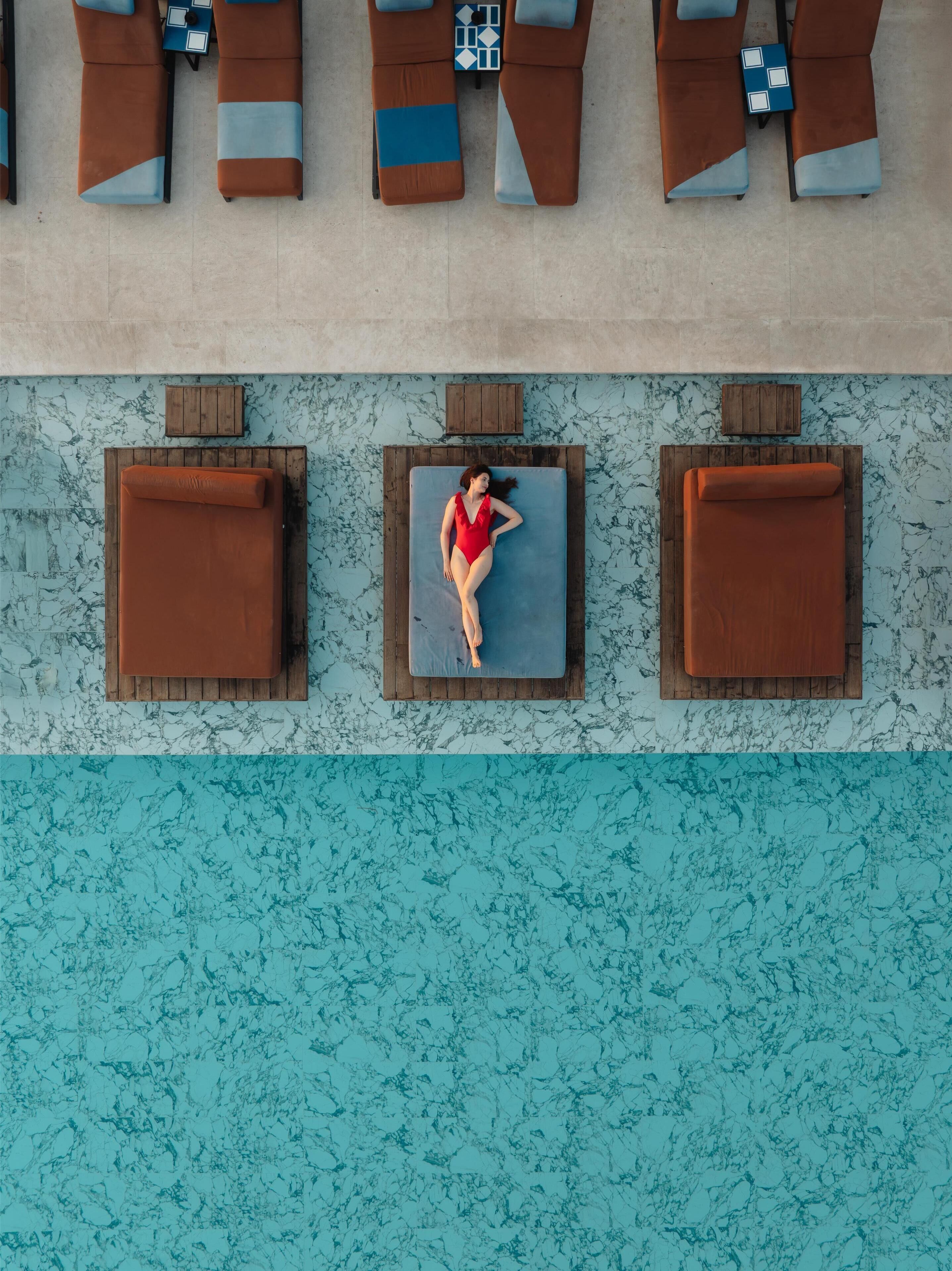 An aerial view of a poolside area with lounge chairs and a person lying on a blue mat.