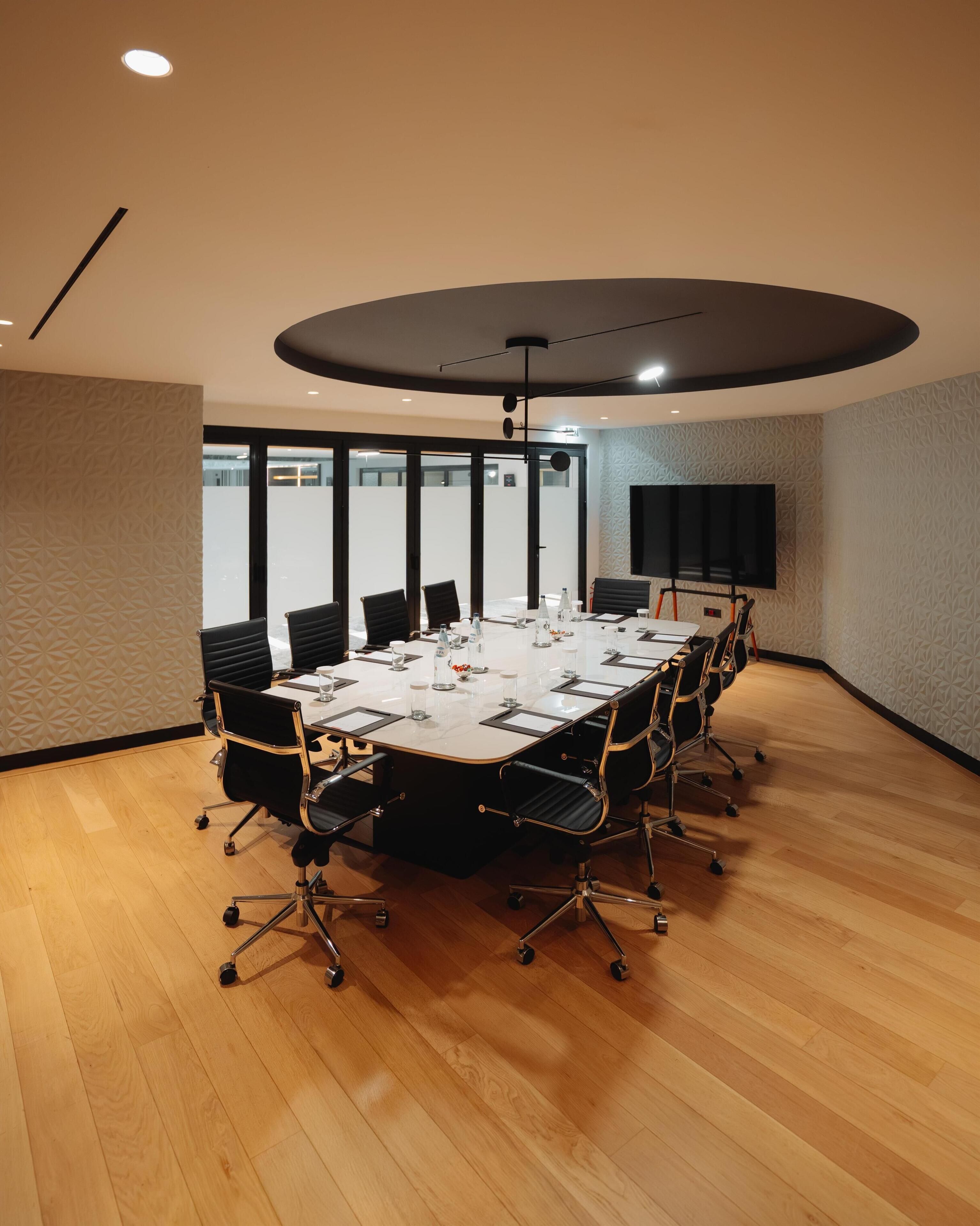 A conference room with a large oval table, black chairs, and a flat-screen TV on the wall.