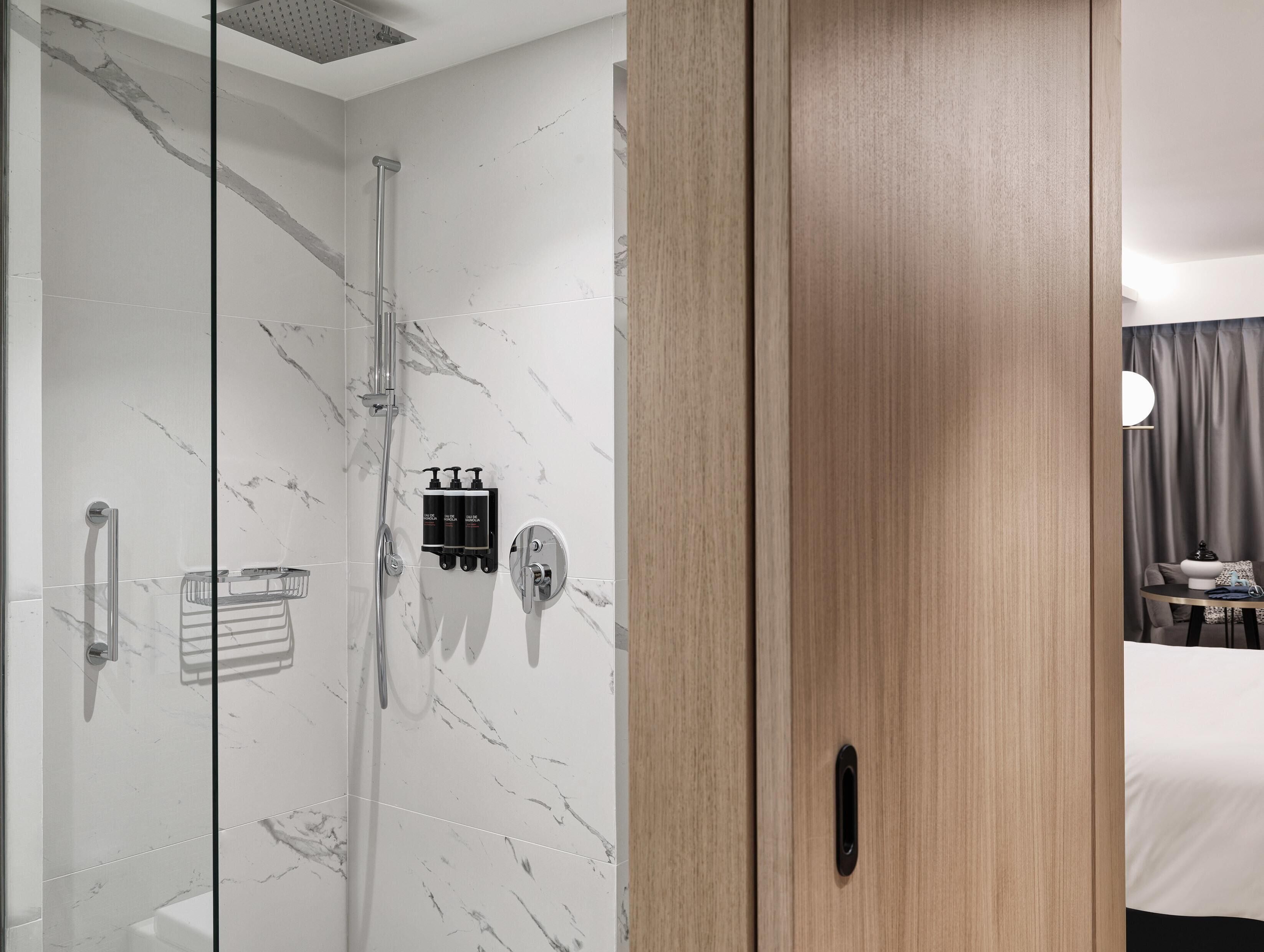 Un bagno moderno con cabina doccia in vetro, pareti in marmo e porta in legno.