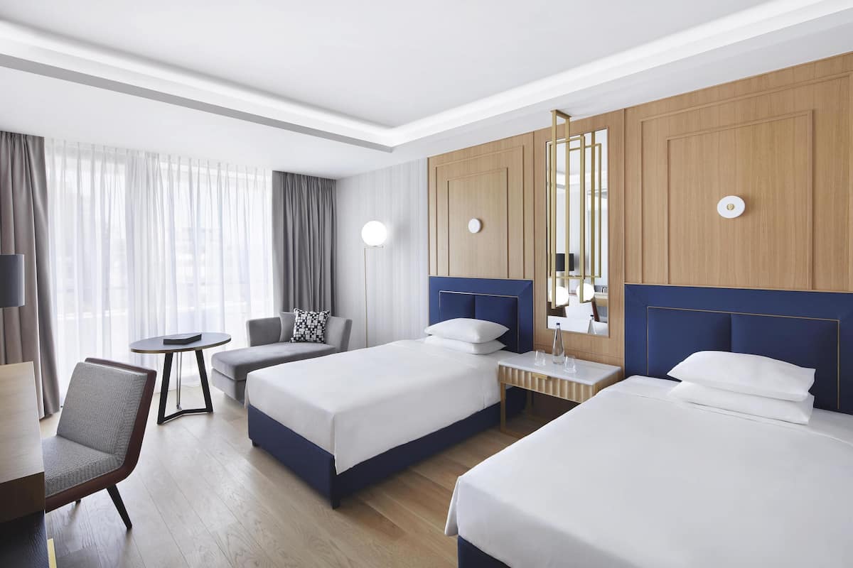 Une chambre d’hôtel avec deux lits, un bureau, une chaise, une petite table et un miroir.