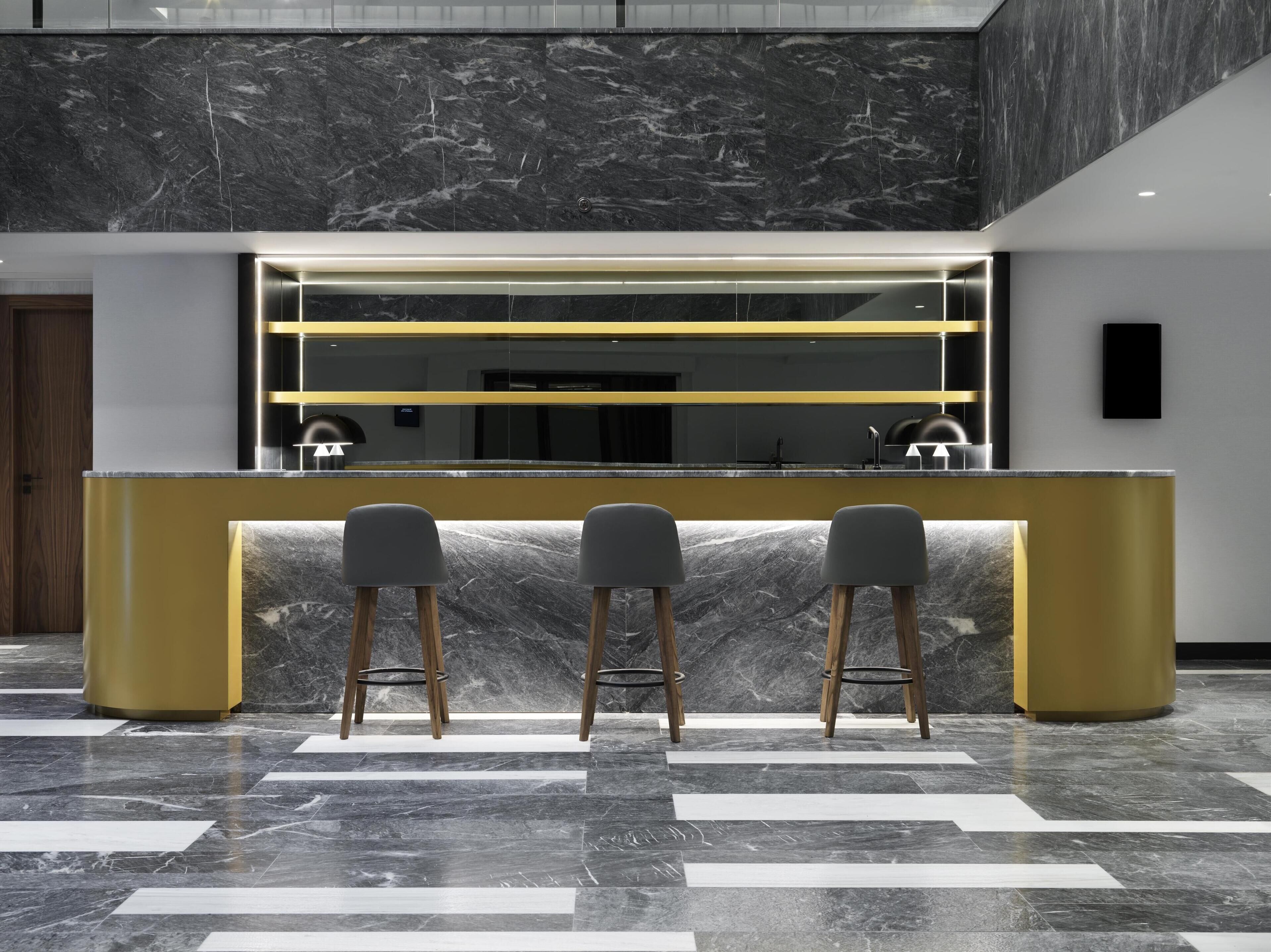 Een moderne bar met een marmeren aanrecht, drie barkrukken en een strakke, verlichte bartop.