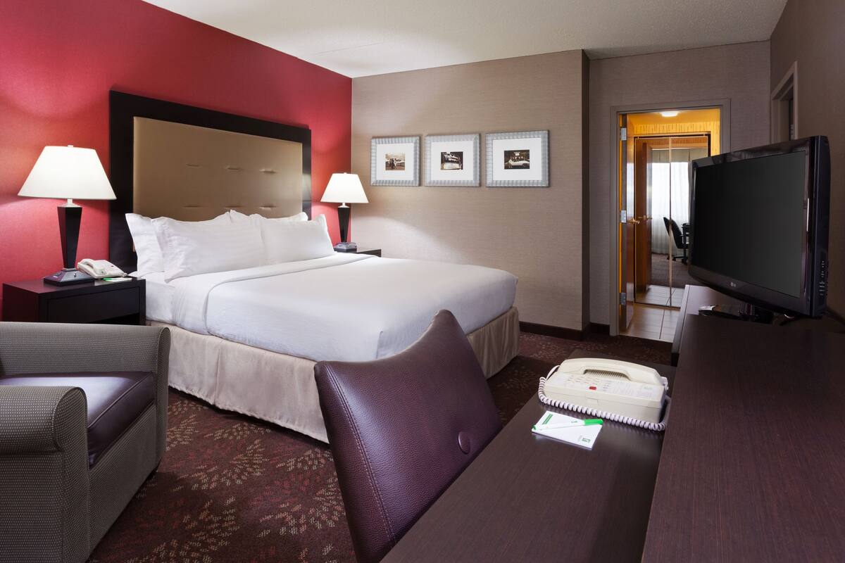 A hotel room with a bed, two bedside tables with lamps, a television, a desk with a telephone, and a chair.