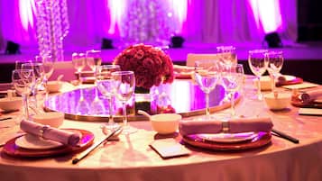 A round table set for dining with wine glasses, bowls, and a centerpiece of red roses.