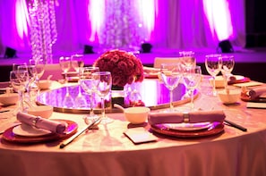 A round table set for dining with wine glasses, bowls, and a centerpiece of red roses.