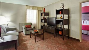 Habitación de hotel con sofá, sillón, televisión y una pequeña mesa con fruta.