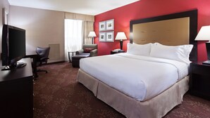 Habitación de hotel con una cama grande, un escritorio con televisor, una silla, una mesita y una lámpara.