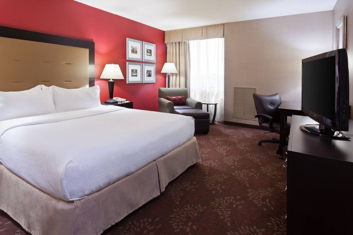 A hotel room with a large bed, a desk, a chair, a TV, and a window with curtains.