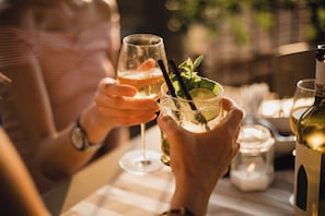A person holding a glass of white wine with a straw, another glass with a lime slice and mint, and a bottle of white wine on a table.