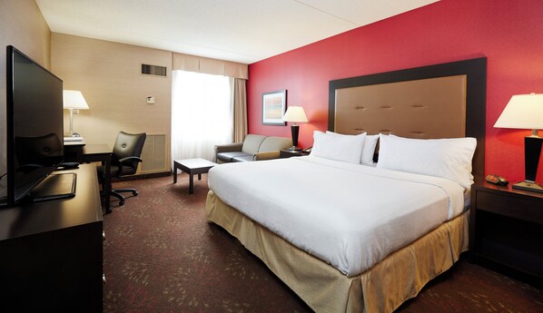 A hotel room with a large bed, a desk with a computer, a chair, a TV, and a window with curtains.