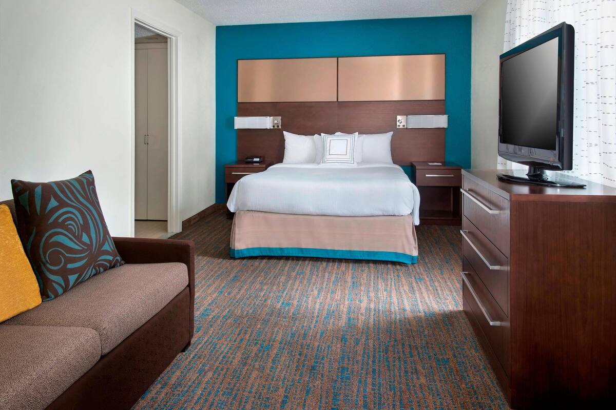 A hotel room with a bed, a TV, a desk, and a sofa.