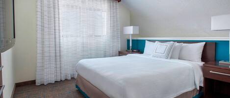 A hotel room with a large bed, a nightstand, a lamp, and a window with curtains.