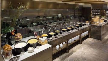 A buffet setup with various food stations and a large kitchen area in the background.