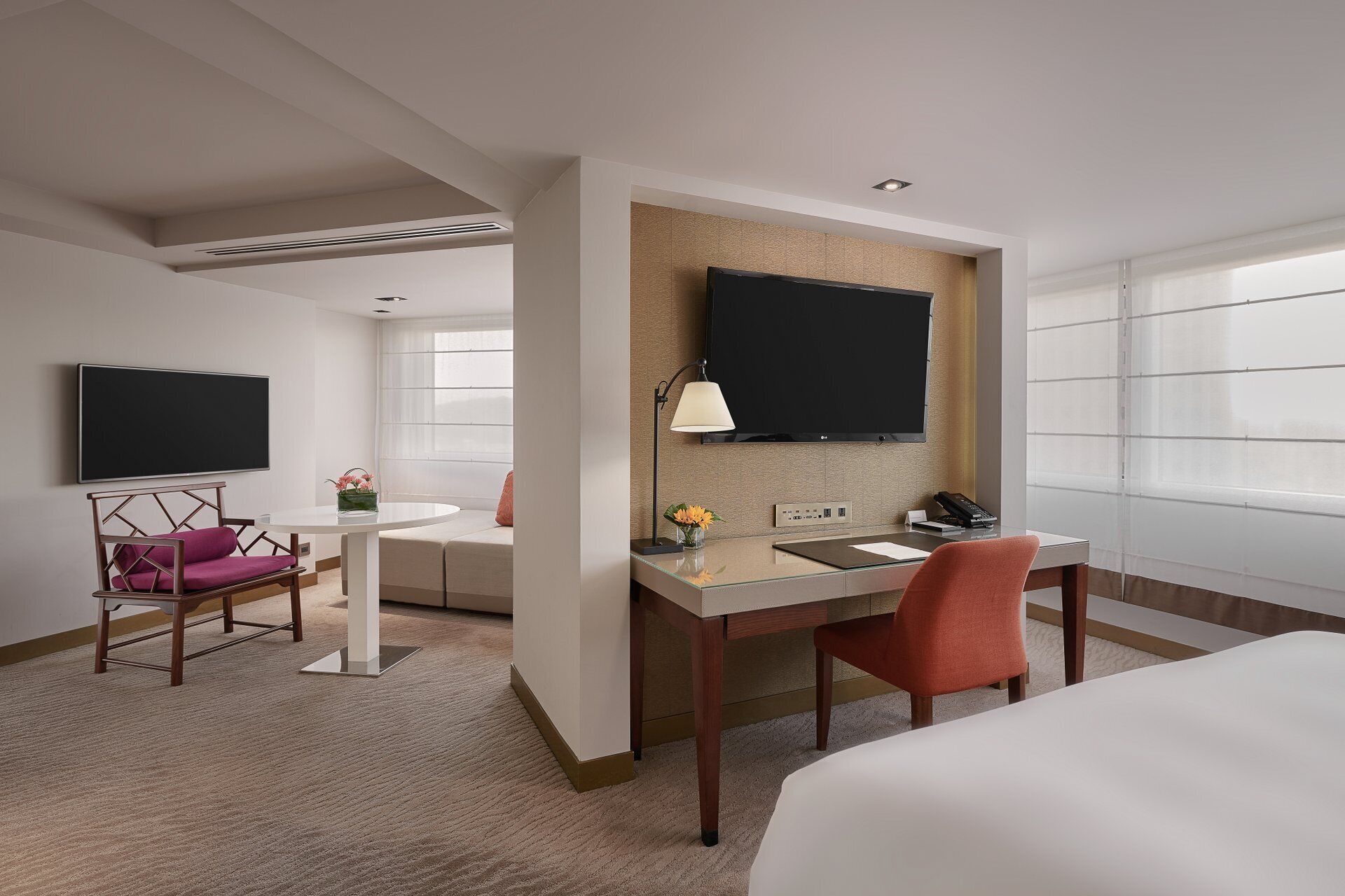 Habitación de hotel con cama, escritorio con silla, televisor en la pared, lámpara y ventana con persianas.