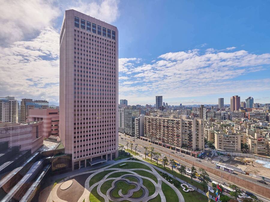 A high-rise building with a grid of windows, surrounded by a landscaped area with pathways and greenery.