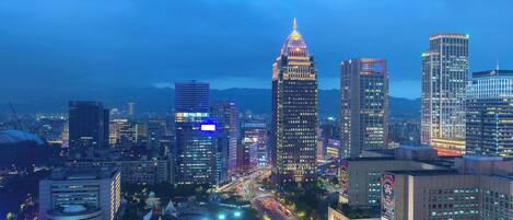A cityscape at dusk with illuminated skyscrapers and a busy street.