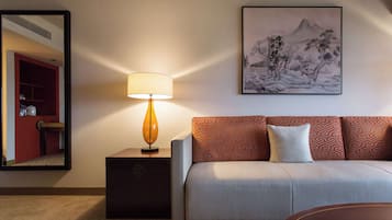 A hotel room with a sofa, a lamp, a framed artwork, and a mirror.