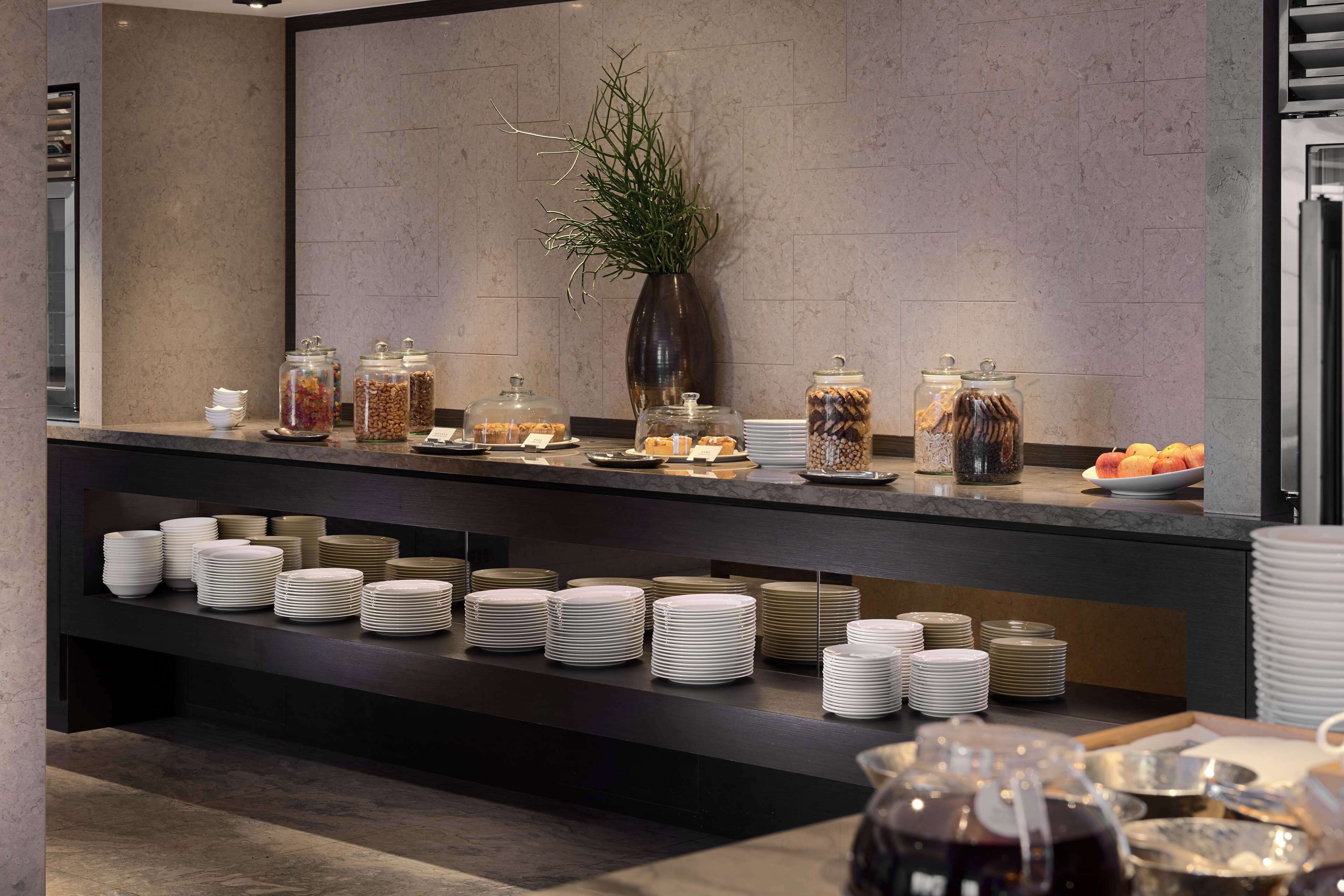 A buffet setup with various food items and utensils, including plates and jars of snacks, arranged on a counter.