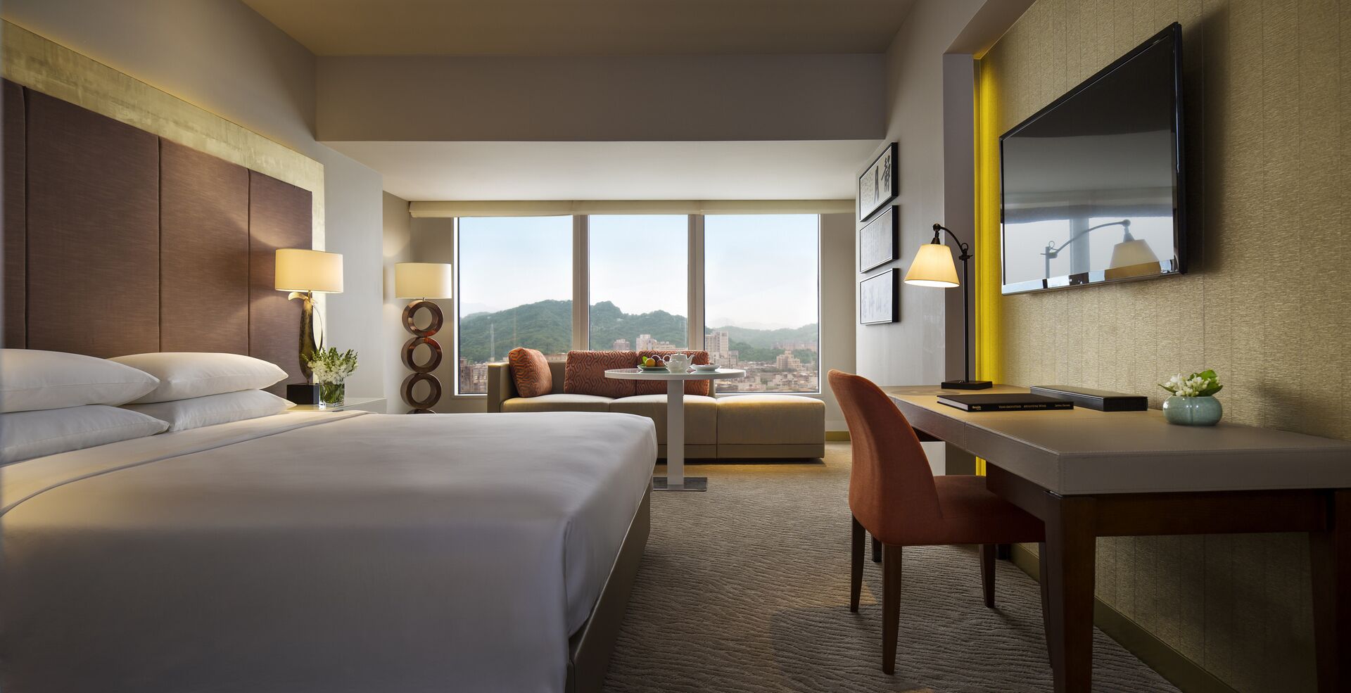 A hotel room with a large bed, a desk, a chair, and a TV.