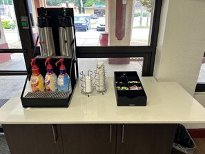 A coffee station with a coffee maker, disposable cups, and coffee creamer bottles. - Red Roof Inn Montgomery - Midtown (Montgomery)