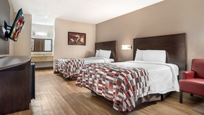 Hotellihuone, jossa on kaksi sänkyä, työpöytä, televisio ja punainen tuoli.