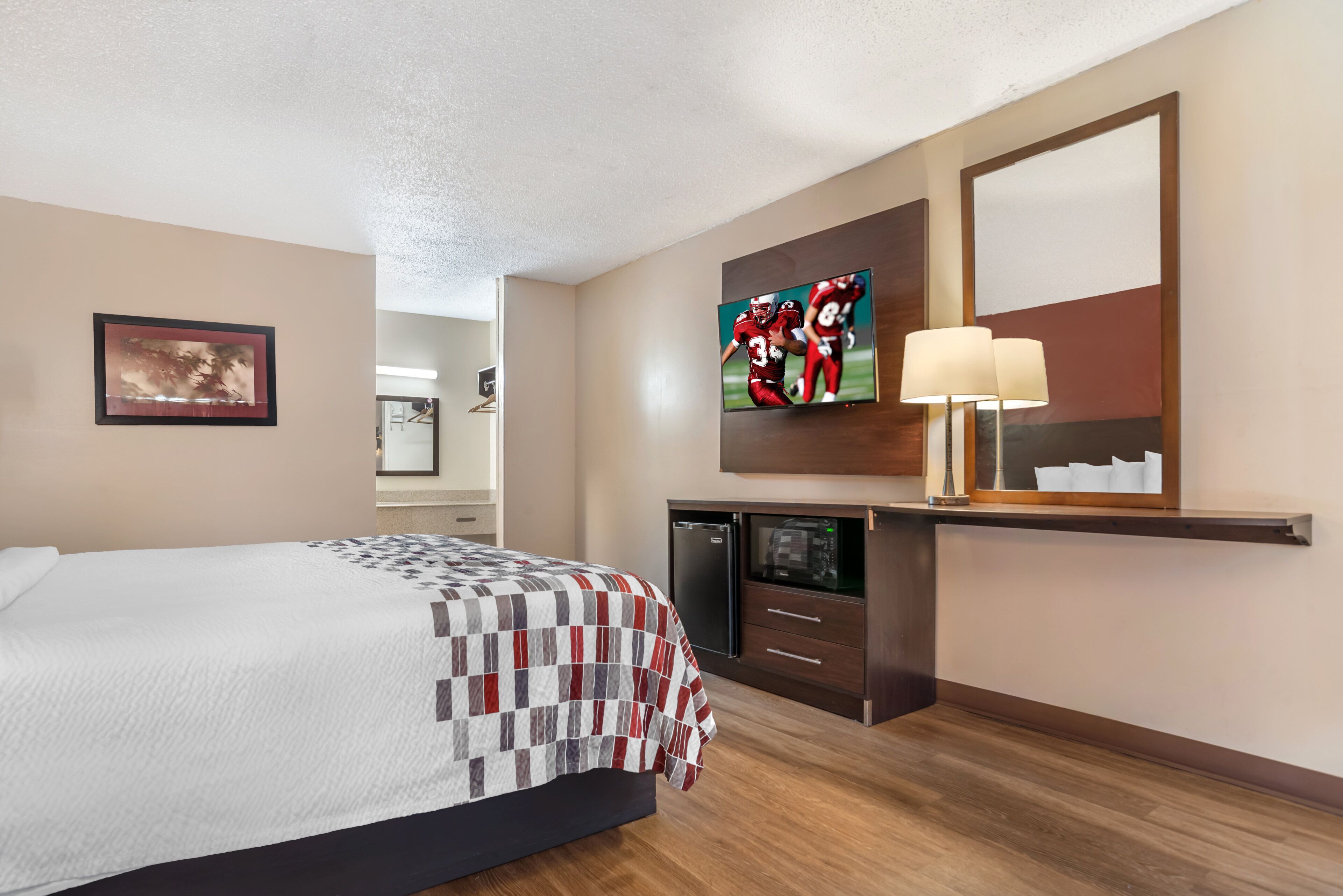 Ein Hotelzimmer mit Bett, Flachbildfernseher, Schreibtisch mit Lampe und Spiegel.
