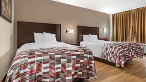 Hotellihuone, jossa on kaksi sänkyä. Jokaisessa sängyssä on puinen pääty, valkoiset vuodevaatteet ja punavalkoinen ruutukuviollinen peitto.