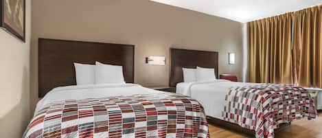 A hotel room with two beds, each with a wooden headboard, white bedding, and a red and white checkered blanket.