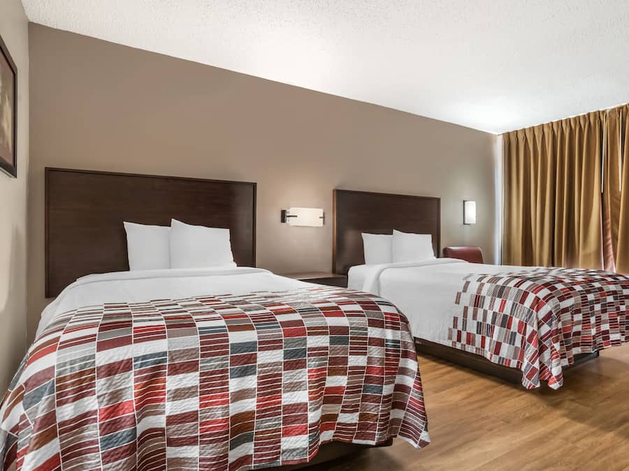 Habitación de hotel con dos camas, cada una con cabecera de madera, ropa de cama blanca y una manta roja y blanca a cuadros.