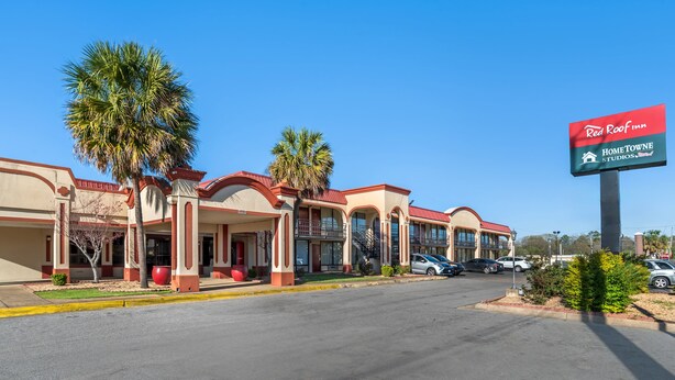 Red Roof Inn -hotelli, jonka yläpuolella on kirkas, sininen taivas. Hotellissa on rivi yhden kerroksen korkuisia rakennuksia, joissa on punaiset katot ja beigen väriset seinät.