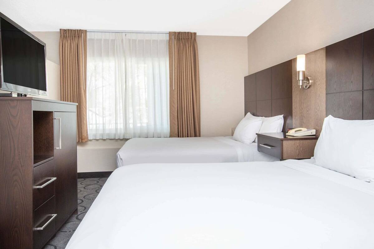 Habitación de hotel con dos camas, un televisor, un escritorio y una ventana con cortinas.