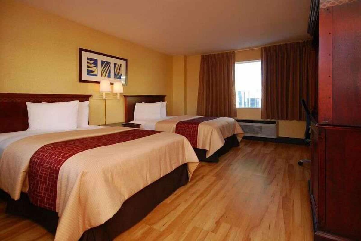 Habitación de hotel con dos camas, un ventanal con cortinas, una obra de arte colgada en la pared y piso de madera.