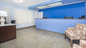 A reception area with a blue counter, a desk with a lamp, and a patterned chair.