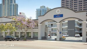 A hotel entrance with a sign reading "BAYMONT INN & RESORTS" and an "ELEVATOR" sign. There are cars parked in front, and a tree with purple flowers to the left.