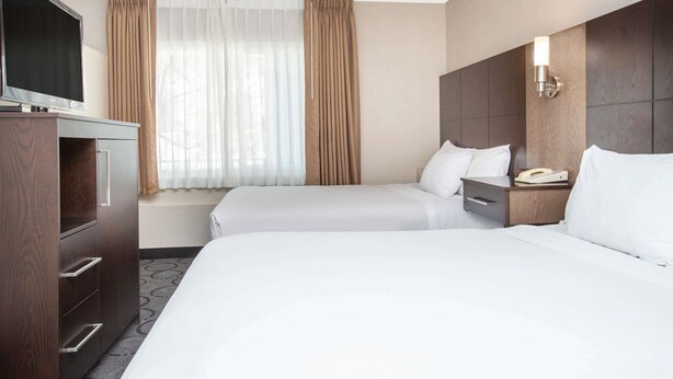 A hotel room with two beds, a TV, a desk, and a window with curtains.