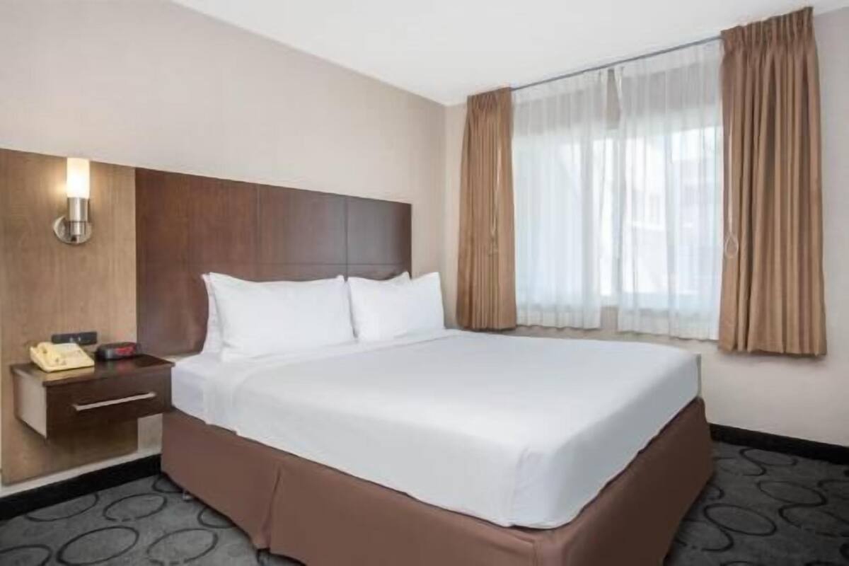 A hotel room with a bed, a nightstand, a telephone, and a window with curtains.