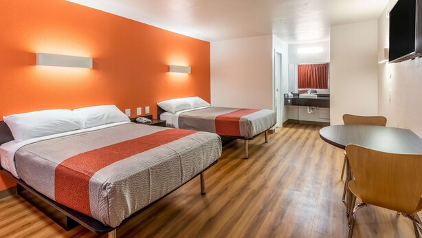 Une chambre d’hôtel avec deux lits, un plancher en bois, une table ronde et une salle de bain visible à travers une porte ouverte.
