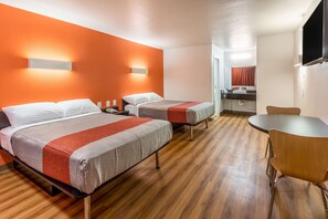 A hotel room with two beds, a wooden floor, a round table, and a bathroom visible through an open door. - Motel 6 Arlington, TX - UTA (Arlington)