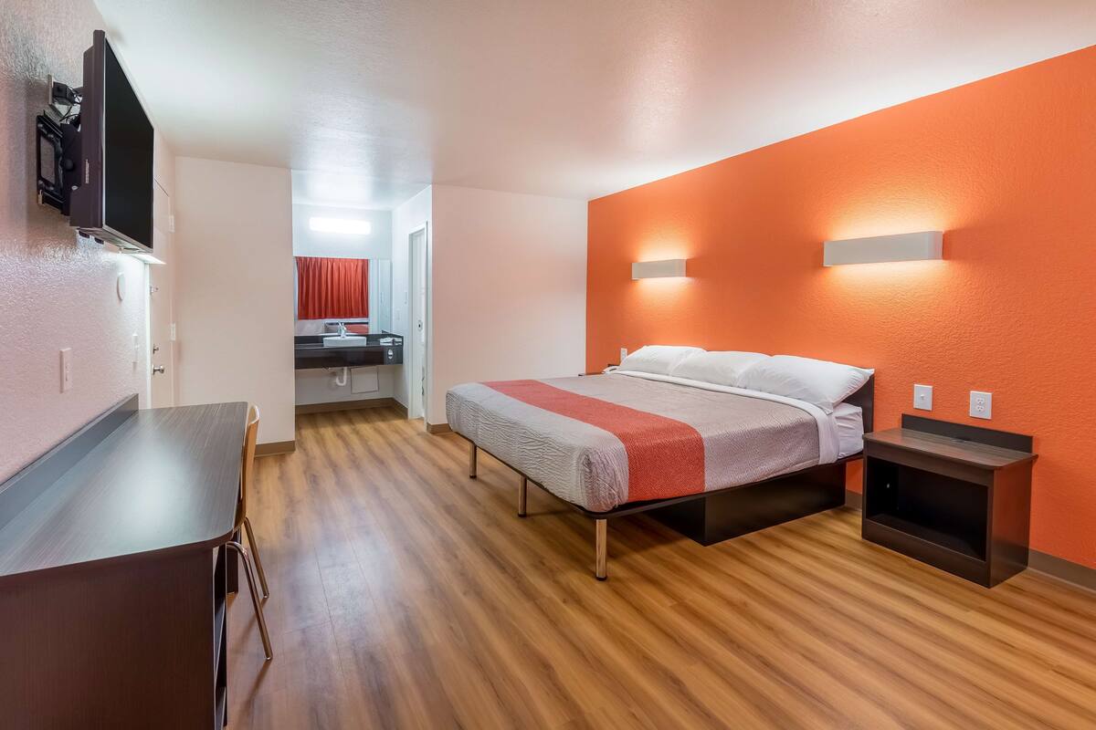A hotel room with a bed, a desk, and a TV mounted on the wall.