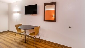 Une chambre d’hôtel avec un plancher en bois, une table ronde, deux chaises, un téléviseur à écran plat et un miroir fixé au mur.
