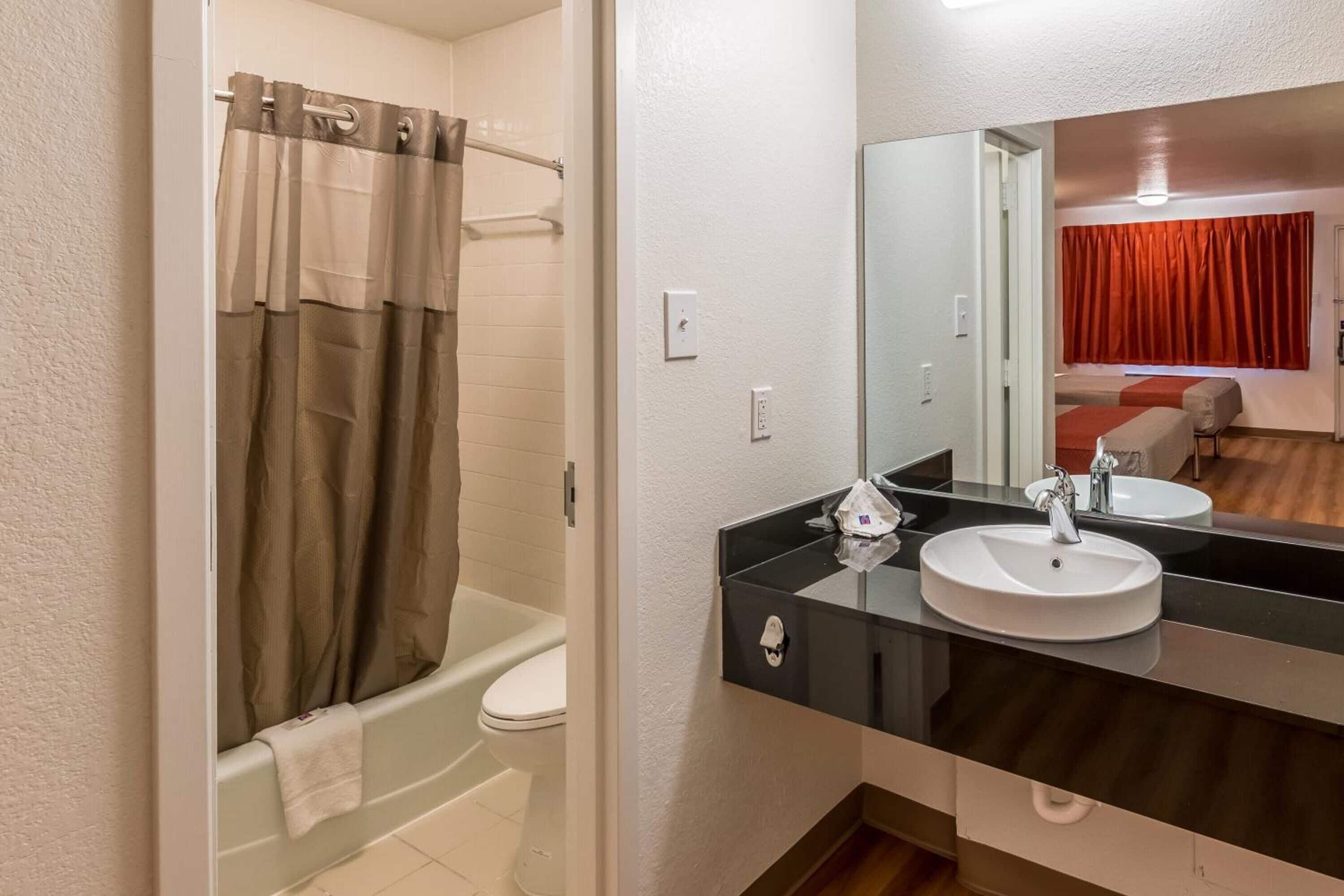 Een badkamer met een bad, een wit toilet, een zwart wastafelmeubel met een spiegel erboven en een rood gordijn op de achtergrond.