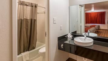 Een badkamer met een bad, een wit toilet, een zwart wastafelmeubel met een spiegel erboven en een rood gordijn op de achtergrond.