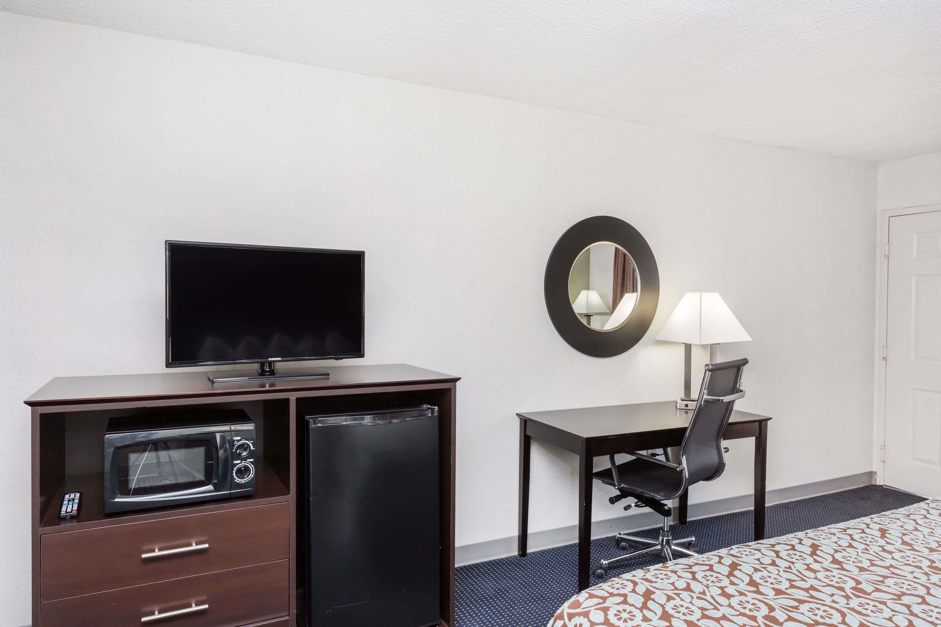 Une chambre d’hôtel comprenant un lit, un bureau avec une chaise, une télévision, un four à micro-ondes, un réfrigérateur et un miroir.