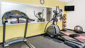Un gimnasio con equipo cardiovascular, un espejo, un reloj y un televisor.