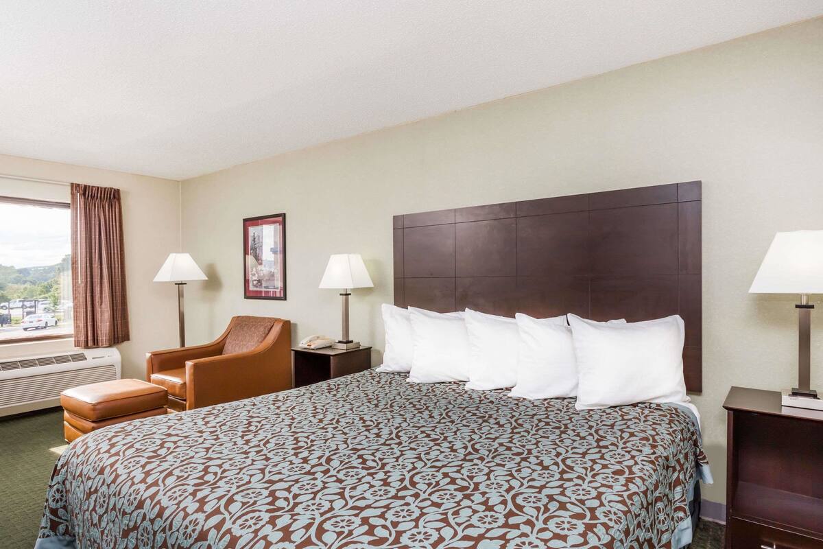 A hotel room with a large bed, two bedside lamps, a chair, a nightstand, and a window with curtains.