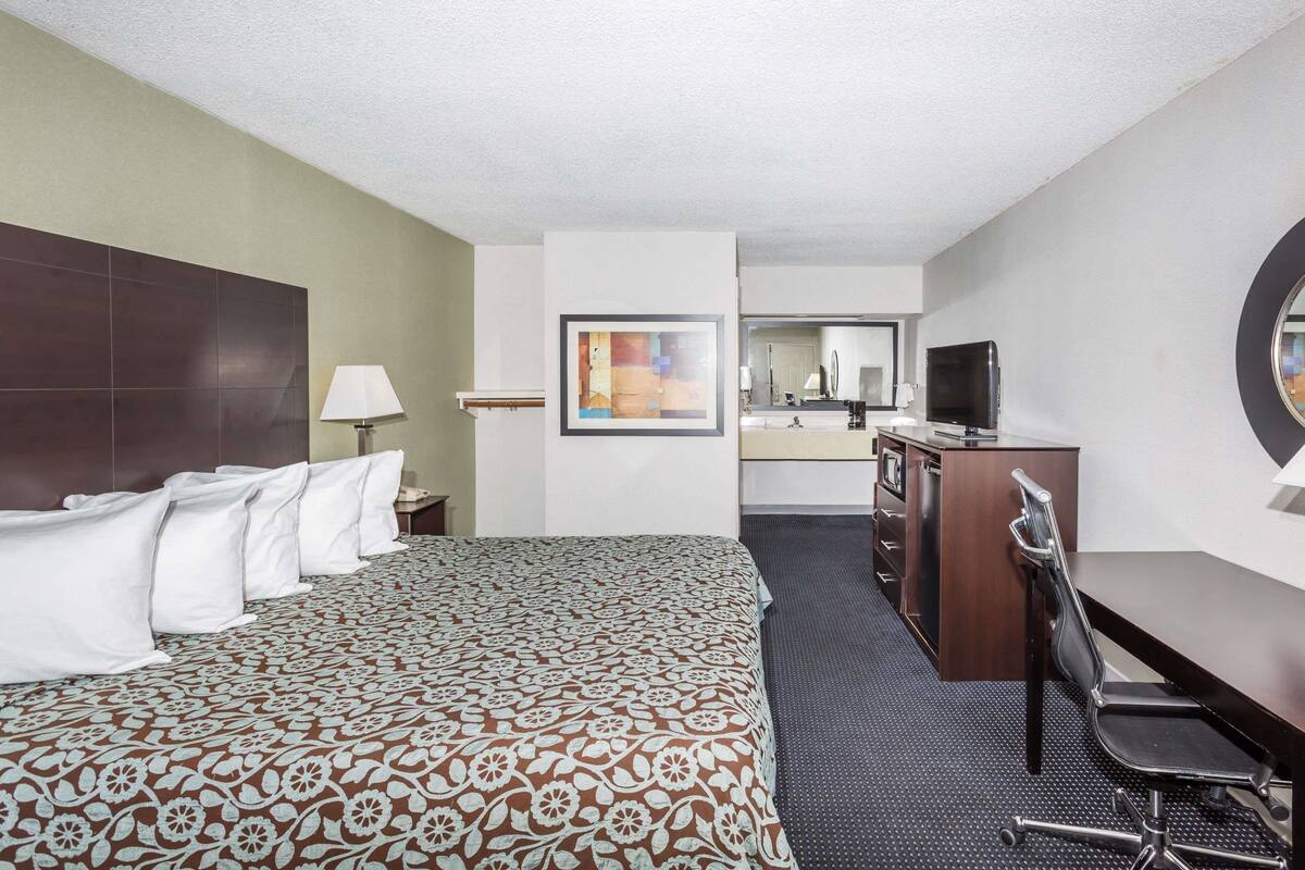 A hotel room with a large bed, a desk with a chair, a television, and a mirror.