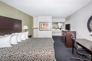 Una habitación de hotel con una cama grande, un escritorio con silla, un televisor y un espejo.